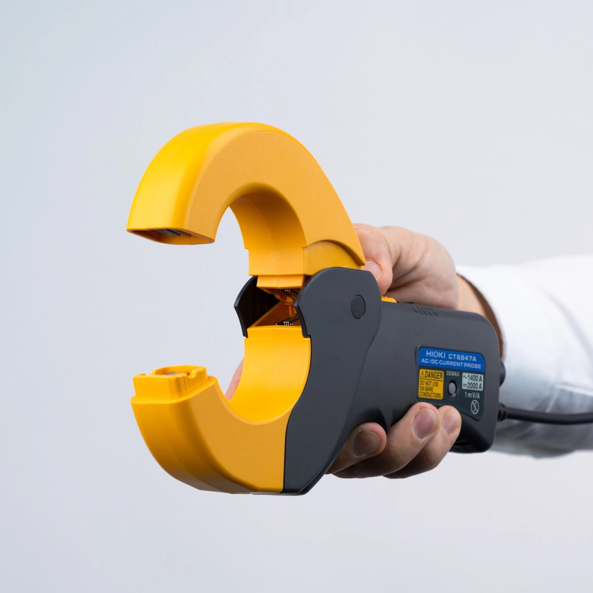 Hand holding a yellow and black clamp meter against a light grey background Hioki CT6847A AC/DC Current Probe