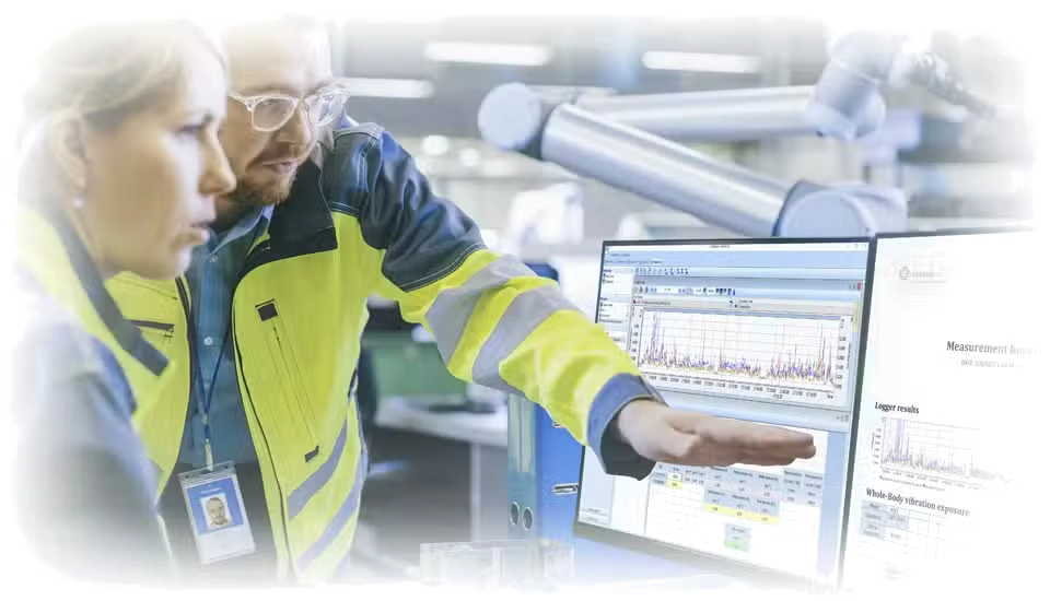Two people in safety vests looking at computer monitors in a factory setting using Svantek Supervisor PC Software for Health and Safety